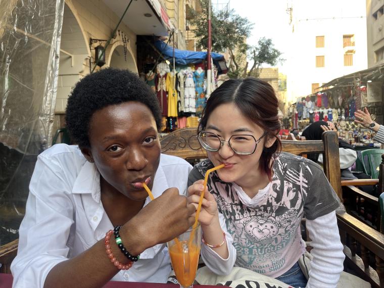 Two Oberlin students sharing mango juice with straws.