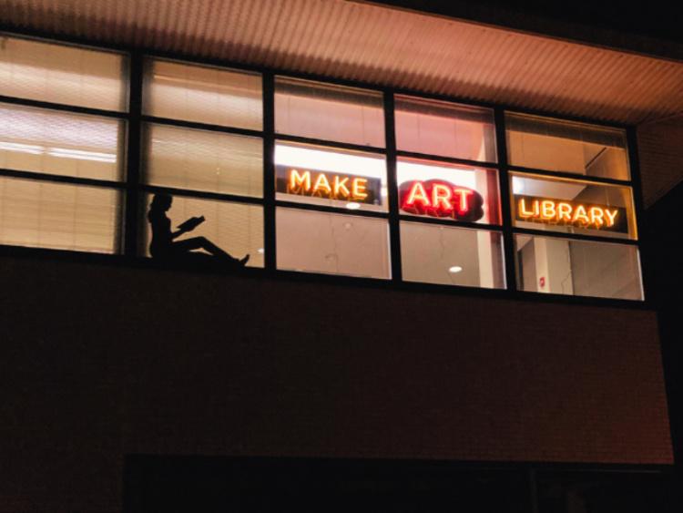 silhouette of student reading, sitting in a window, lit from behind 