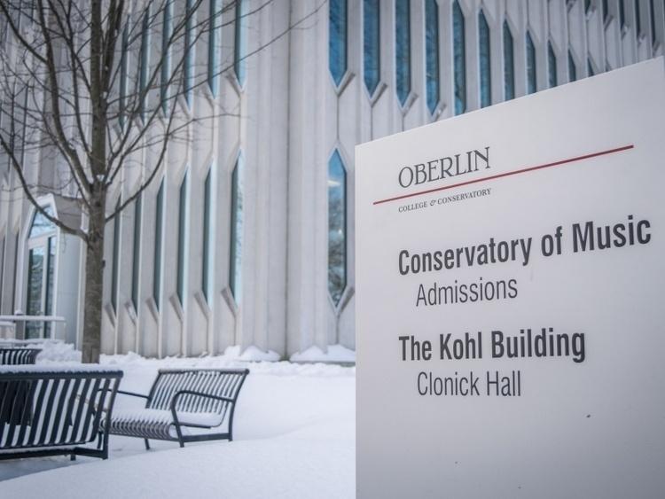 Sign listing the Conservatory of Music Admissions Office, the Kohl Building, and Clonick Hall. Snowy campus background.