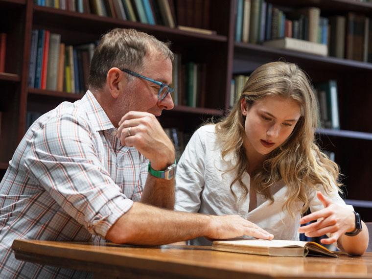 a student and professor study a book