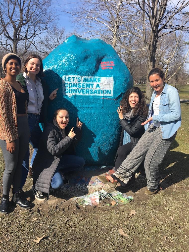 Five students in front of a blue painted rock