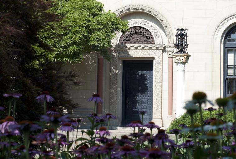 Entry door to building framed by tree and flowers.