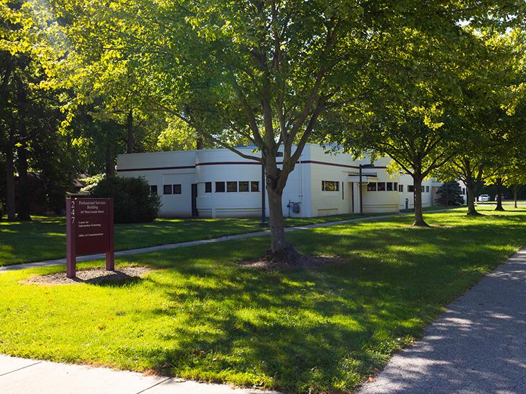 Exterior of a single-level office building behind a lawn and tree.