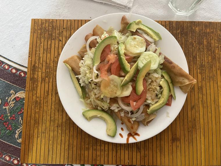 A meal of taquitos, vegetables, and avocado.