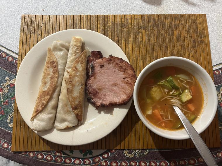 A meal of taquitos, pork, and a vegetable soup.